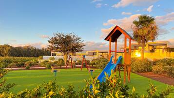 A playground with a slide and swings, surrounded by well-maintained grass and trees.