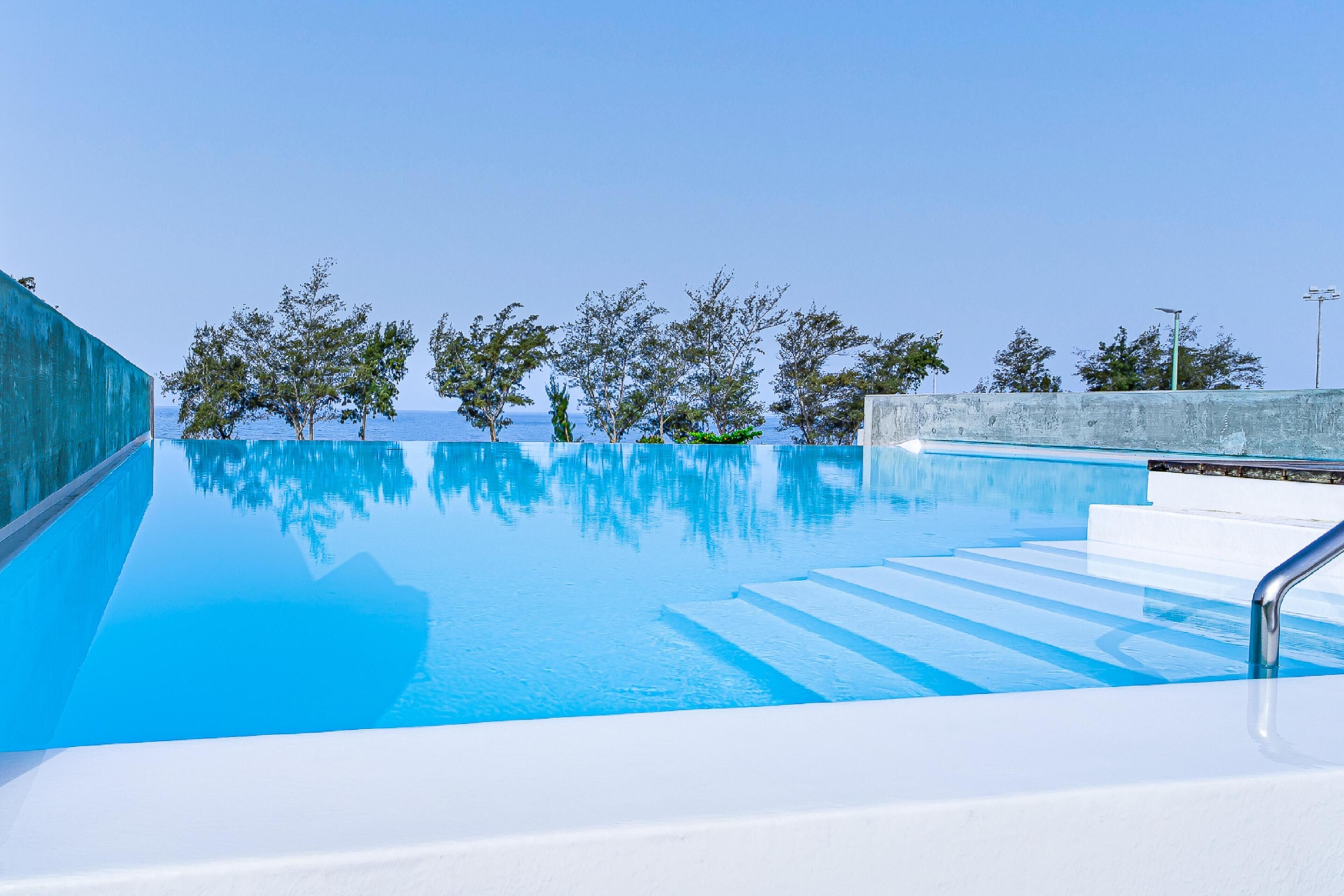A clear blue swimming pool with steps leading into it, surrounded by trees and a clear sky.