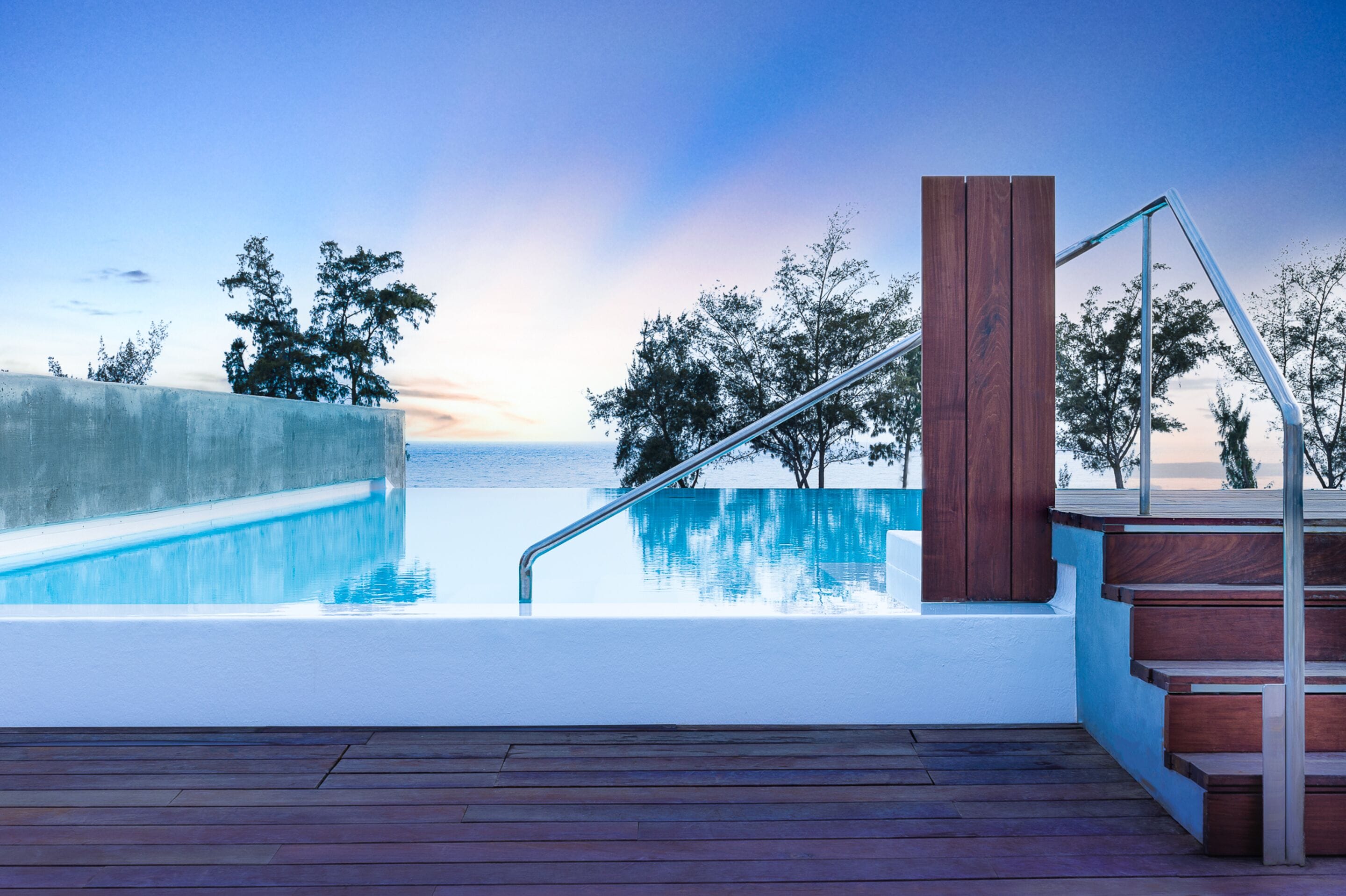 Una piscina con cubierta de madera y escaleras que llevan a un balcón con vistas al mar.