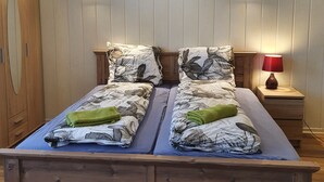 Ein Doppelbett mit floralem Überwurf, ein Nachttisch mit roter Lampe und ein Gemälde einer Küstenlandschaft darüber.
