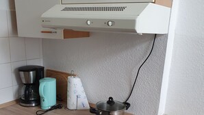 Eine kompakte Küche mit einem Herd, einem Backofen, einem Wasserkocher und einem Topf auf einer Induktionskochplatte.
