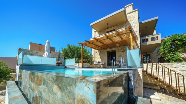 A modern outdoor pool area with a stone wall, a pergola, and a staircase leading to a second level. - Asion Suite Eros with Private Pool (Kato Asites)