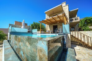 Ein moderner Poolbereich im Freien mit einer Steinwand, einer Pergola und einer Treppe zu einer erhöhten Ebene.