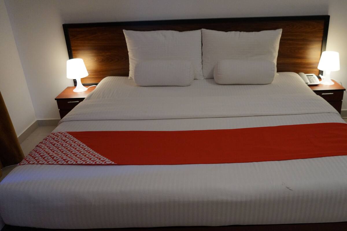 A large bed with white linens, two bedside lamps, and a red throw blanket.