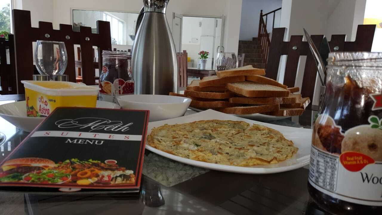 Una mesa de desayuno con un menú, un tarro de mermelada, una tostada en un plato y un vaso de agua.