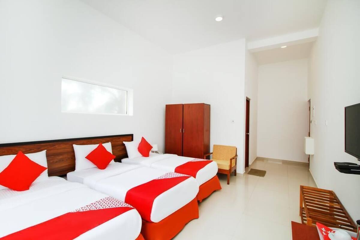 A hotel room with two beds, a wooden wardrobe, a television, and a window.