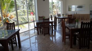 A spacious dining area with large windows, wooden furniture, and a view of palm trees. - Meth Suites (Uswetakeiyawa)
