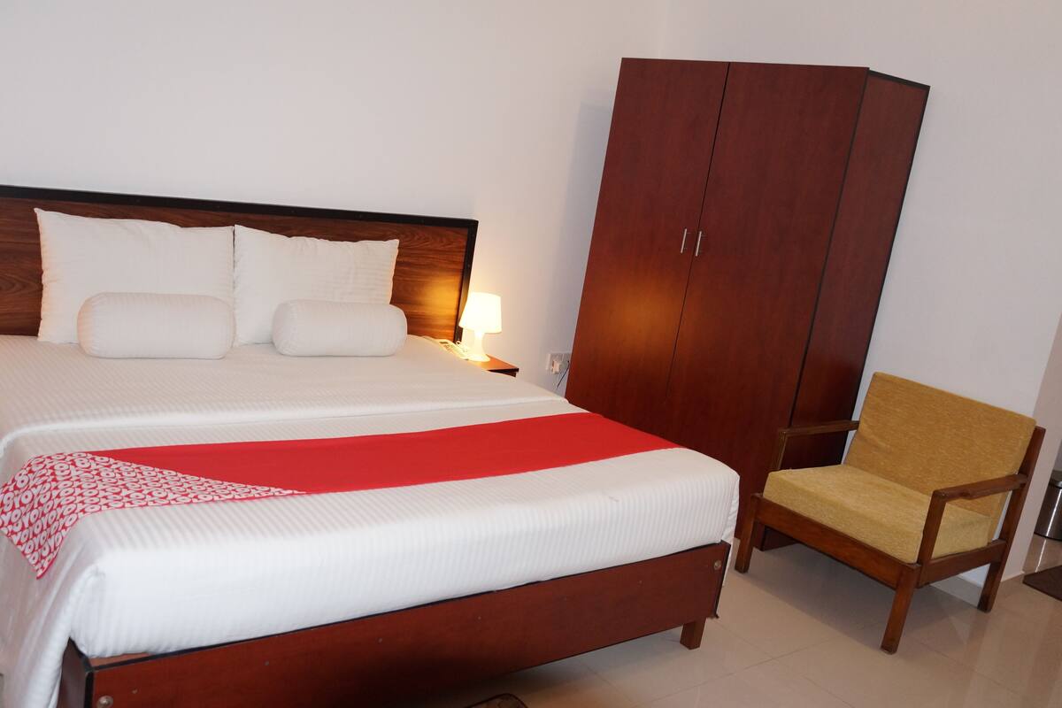 A hotel room with a large bed, two bedside lamps, a wooden wardrobe, and a wooden chair.