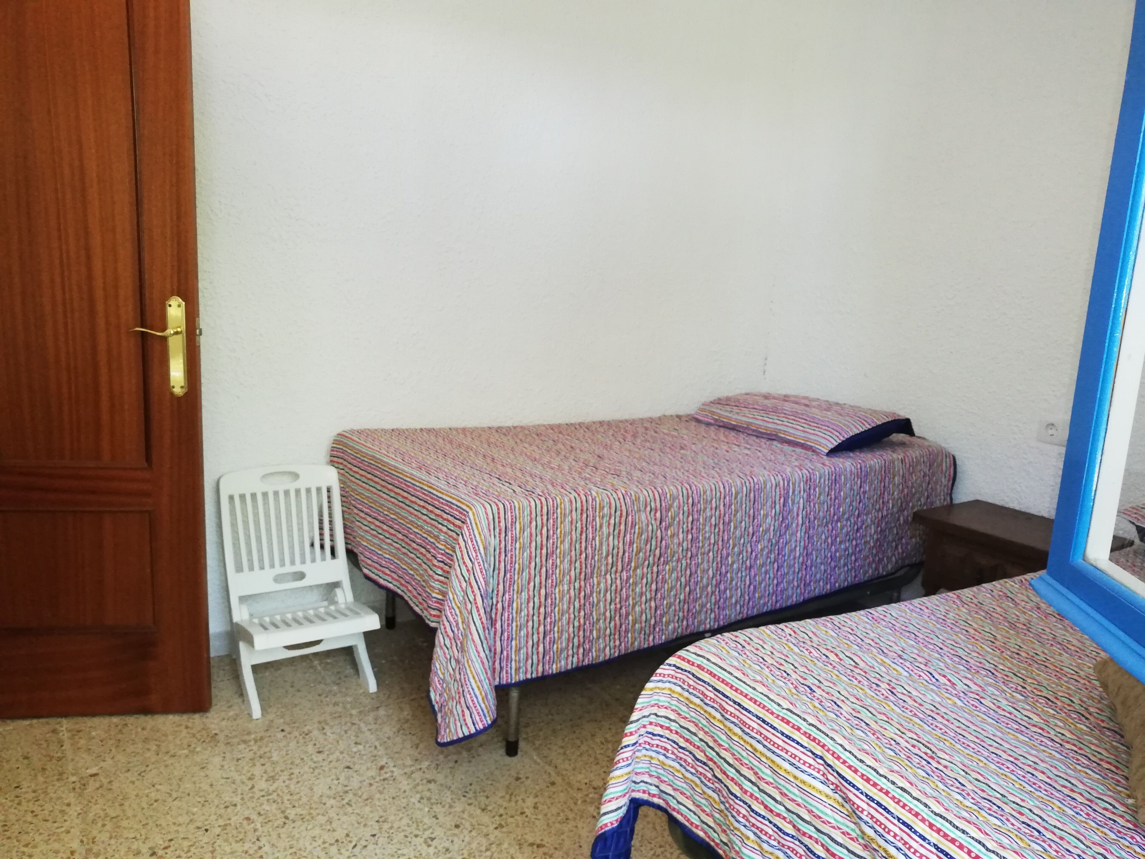 A small room with two single beds, a white chair, and a wooden door.