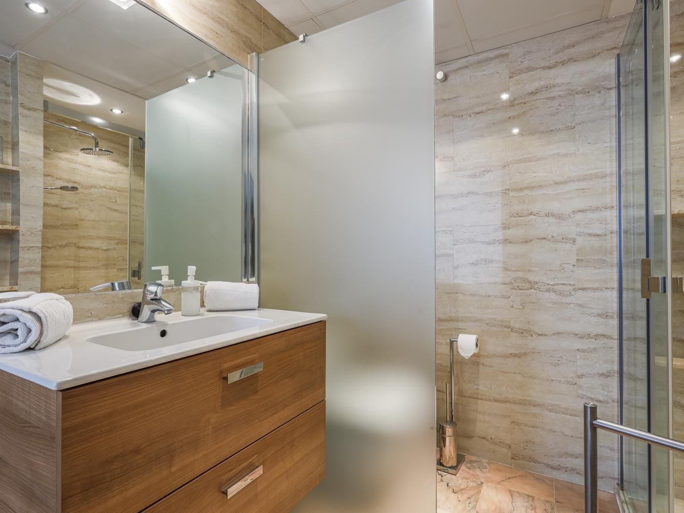 Een moderne badkamer met een houten wastafel, een grote spiegel en een douchecabine van glas.