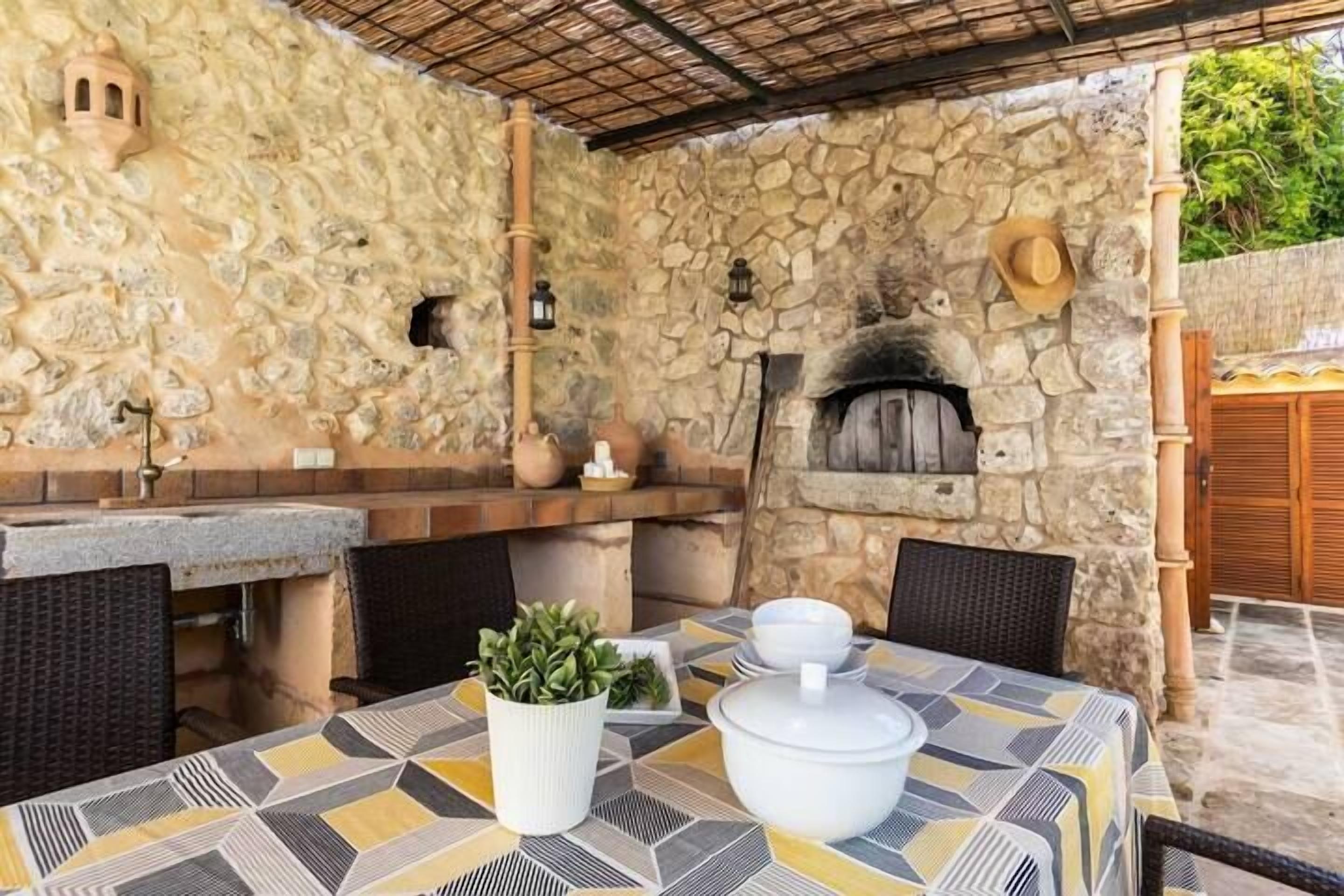 Eine Terrasse im Freien mit Steinmauer, Pizzaofen und Tisch, gedeckt mit Schüsseln und einer Topfpflanze.