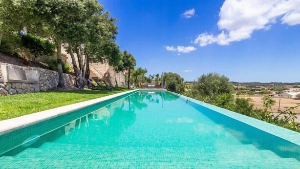 Une piscine rectangulaire à l’eau d’un bleu cristallin, entourée d’un mur de pierre et d’une végétation luxuriante.