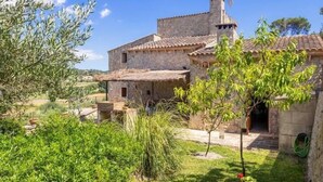 Un bâtiment en pierre, surmonté d’un toit en tuiles, entouré de verdure et baigné par un ciel dégagé.