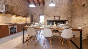 Une cuisine moderne avec des murs en pierre, des poutres en bois et un coin repas comprenant des chaises blanches et une table dressée pour quatre personnes.
