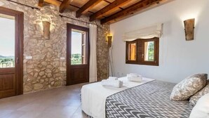 Une chambre avec des murs en pierre, des poutres apparentes, un lit avec une literie à motifs et une vue sur l’extérieur.