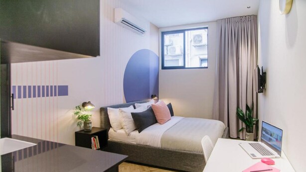 A modern bedroom with a bed, bedside table, lamp, and a desk with a laptop.
