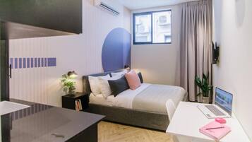 A modern bedroom with a bed, bedside table, lamp, and a desk with a laptop.