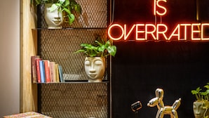 A reception desk with a neon sign stating "RECEPTION IS OVERRATED" and a metal mesh partition with potted plants and books. - Colorbox Ben Yehuda - Smart Hotel by Loginn Tel Aviv (Tel Aviv)