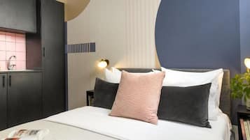 Una habitación de hotel con cama, mesita de noche con planta, y lámpara fijada a la pared.