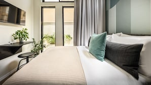 A modern hotel room with a large bed, a flat-screen TV, a small table with a plant, and a view of the outdoors through large windows. - Colorbox Ben Yehuda - Smart Hotel by Loginn Tel Aviv (Tel Aviv)
