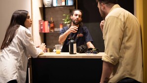 A bar area with a counter, a camera, a bottle, and a drink. - Colorbox Ben Yehuda - Smart Hotel by Loginn Tel Aviv (Tel Aviv)