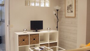A living room with a TV on a white stand, a glass coffee table, and a sofa. - Central and cozy apartment in Seville - Wifi (Sevilla)
