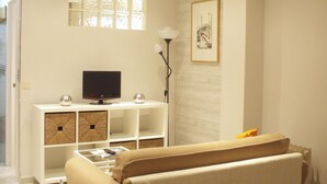 A living room with a flat-screen TV on a white console, a sofa, and a framed picture on the wall. - Central and cozy apartment in Seville - Wifi (Sevilla)