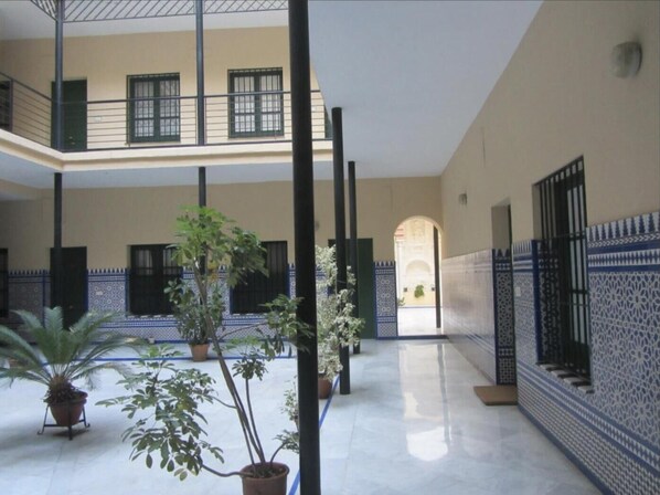 Stunning courtyard with high ceilings, mezzanine level, and potted plants, surrounded by intricate tile patterns and polished stone tiles.