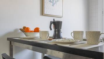 Uma bancada de cozinha com uma cafeteira, uma tigela de laranjas e duas canecas.