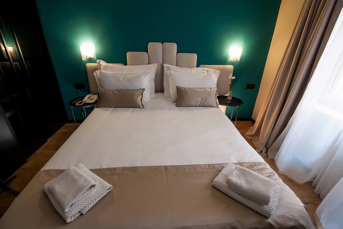 Une chambre d’hôtel avec un grand lit, deux tables de chevet, un téléphone et des lampes fixées au mur.