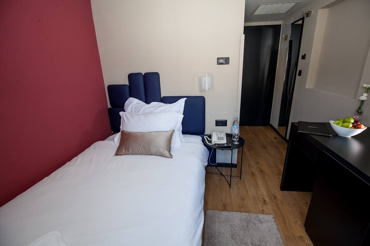 Une chambre d’hôtel avec un lit, un bureau, un téléphone, une bouteille d’eau et un bol de fruits.