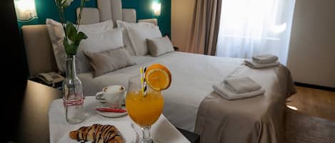 A hotel room with a neatly made bed, a breakfast table with croissant and orange juice, and a vase with flowers.