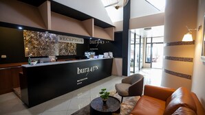 Un hall d’hôtel moderne avec un comptoir noir, un bureau d’accueil et un espace détente comprenant un canapé en cuir marron et une table basse ronde.