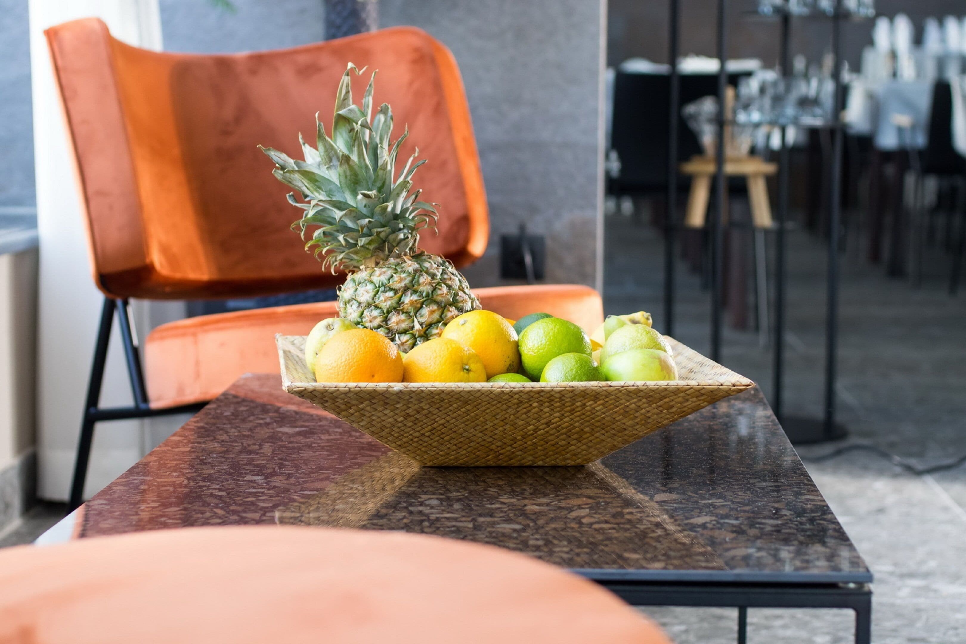 A wicker fruit bowl on a marble table with a pineapple, lemons, and limes.