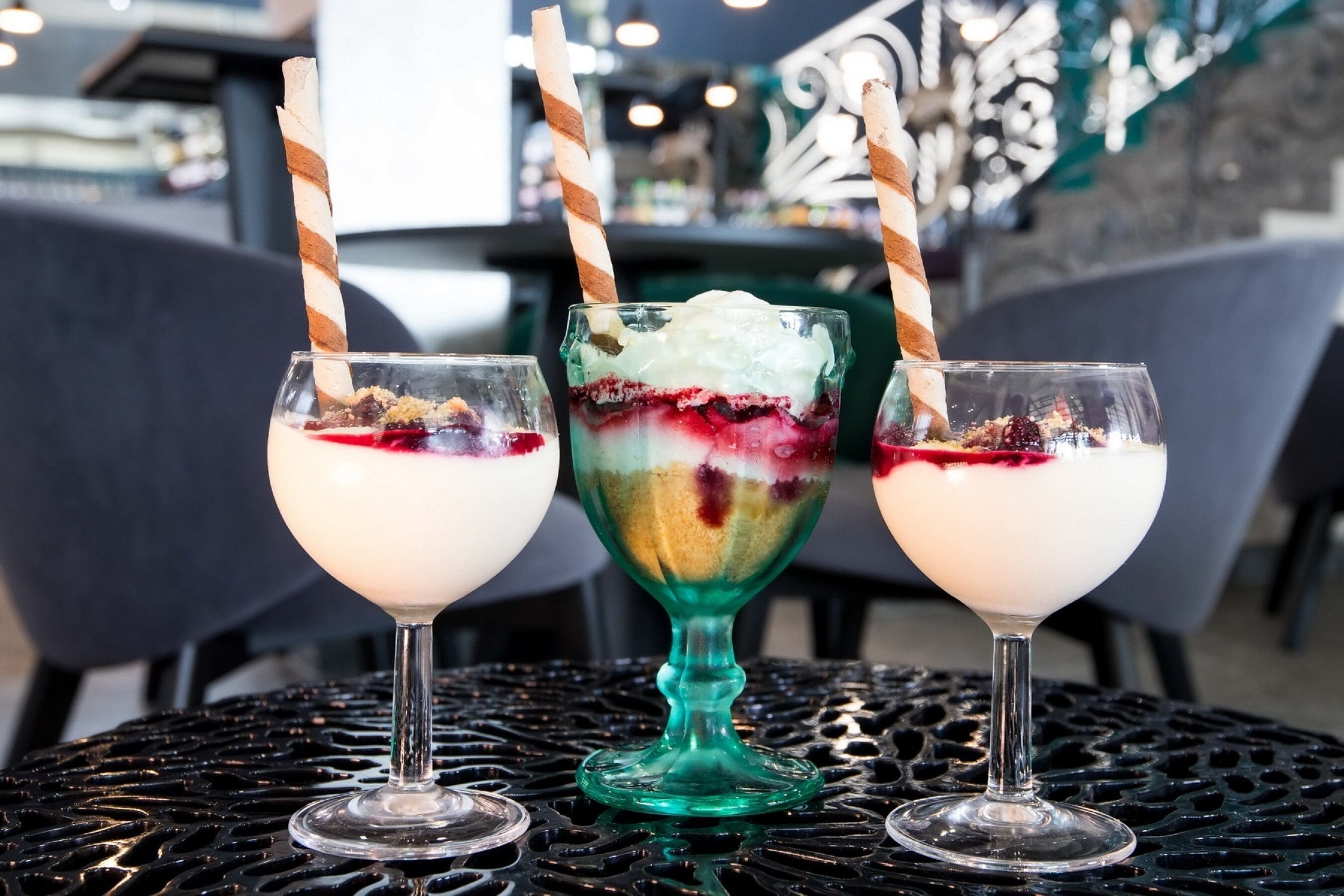 Trois verres à dessert avec des pailles rayées, posés sur une table en métal.
