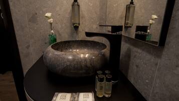 A bathroom with a large stone sink, a mirror, and toiletries on the counter.