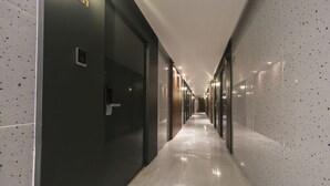 Un pasillo moderno de hotel con piso de mármol pulido, paredes oscuras y varias puertas que dan a las habitaciones.