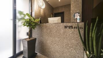 A reception desk with a sign reading "N°25 HOTEL" and a potted plant to the left.