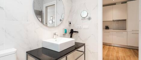 A modern bathroom with a white marble wall, a round mirror, a black countertop, and a white sink.