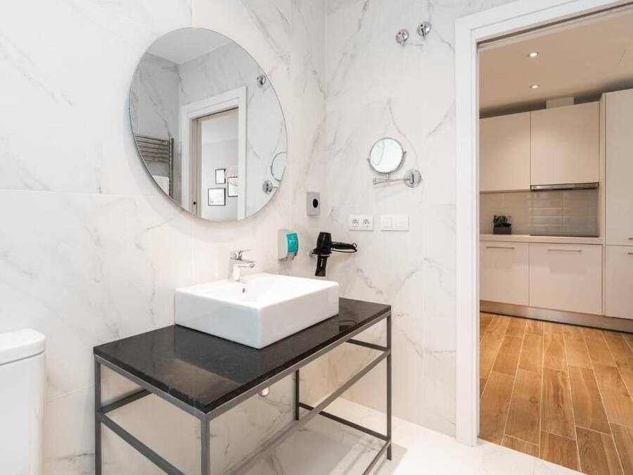 Un baño moderno con pared de mármol blanco, espejo redondo, encimera negra y lavamanos blanco.