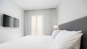 A hotel room with a large bed, a flat-screen TV mounted on the wall, and a window with sheer curtains. - Tandem Puerto Chico (Cádiz)