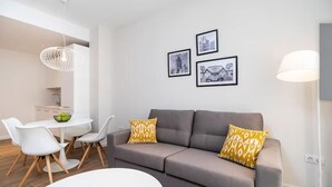A modern living room with a grey sofa, white chairs, and a dining table. There are three framed pictures on the wall and a floor lamp. - Tandem Puerto Chico (Cádiz)