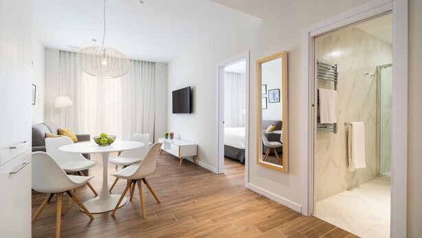 A modern hotel room with a dining area, a large mirror, a shower, and a television. - Tandem Puerto Chico (Cádiz)