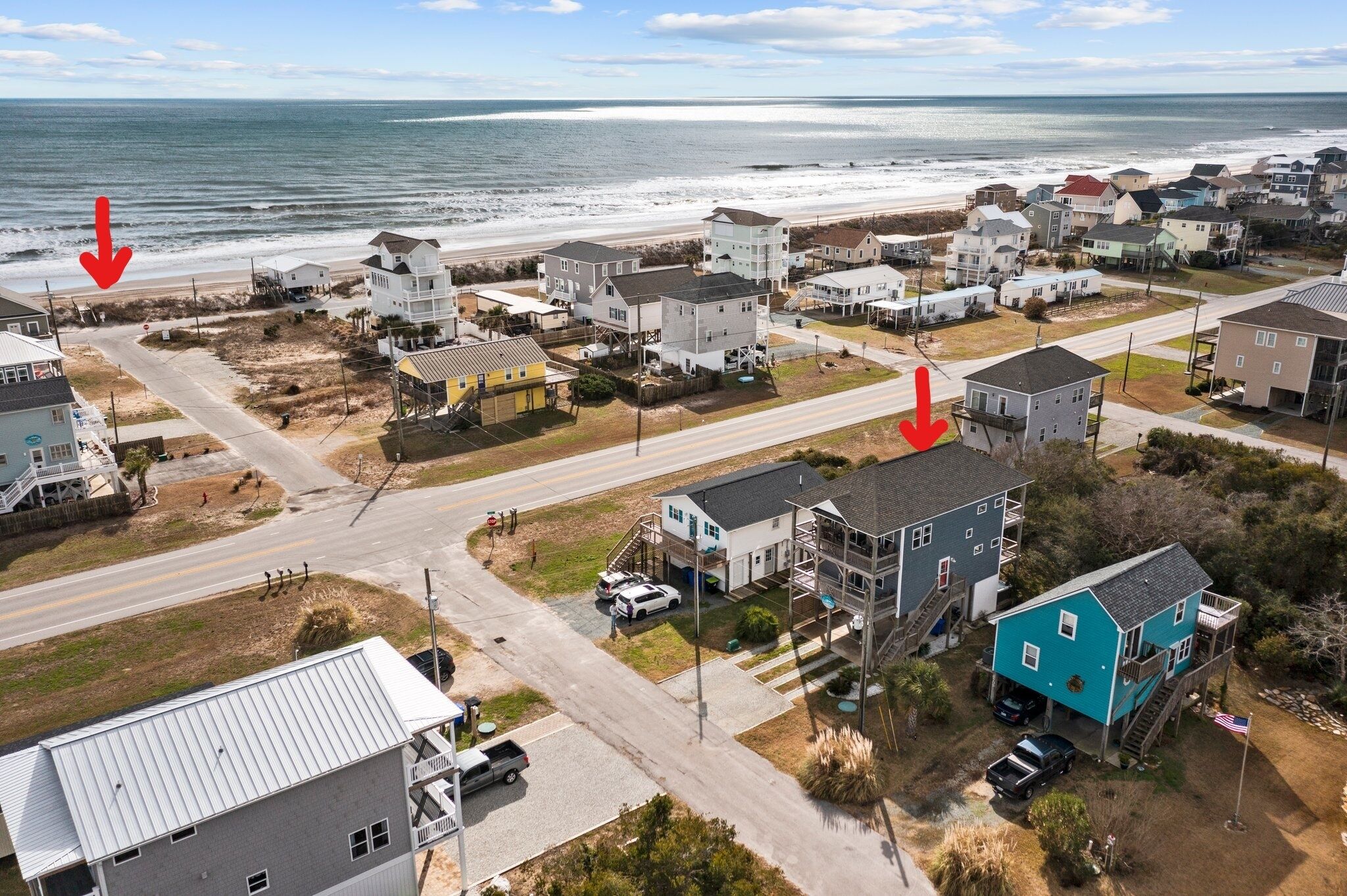 An aerial view of a coastal residential area with houses, a road, and a beach.