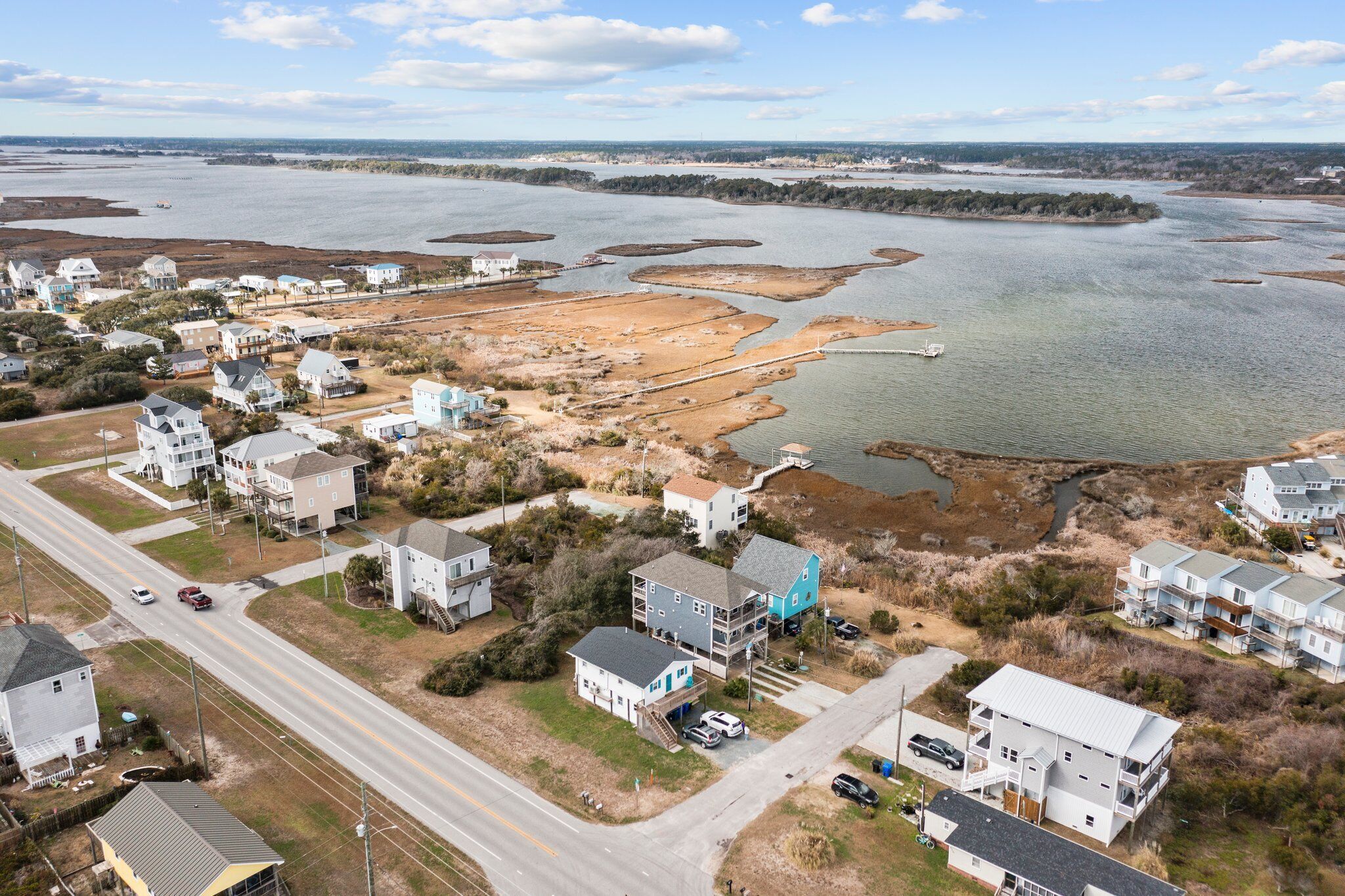 An aerial view of a coastal residential area with houses, a road, and a large body of water.