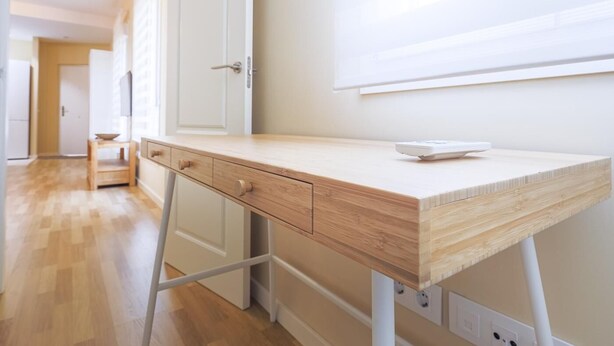 Une pièce moderne équipée d’un bureau en bois, d’un tableau blanc et d’une petite table sur laquelle se trouve un bol.