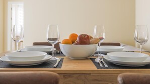 Une table à manger est dressée avec de l’argenterie blanche, des couverts et des verres, et un saladier rempli de fruits et de biscuits est placé au centre.