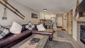 A living room with a brown leather sofa, a coffee table, and a fireplace. There is a kitchen in the background with white cabinets and a refrigerator. - C212 Cinnamon Ridge 2 Bedroom Condo by RedAwning (Keystone)