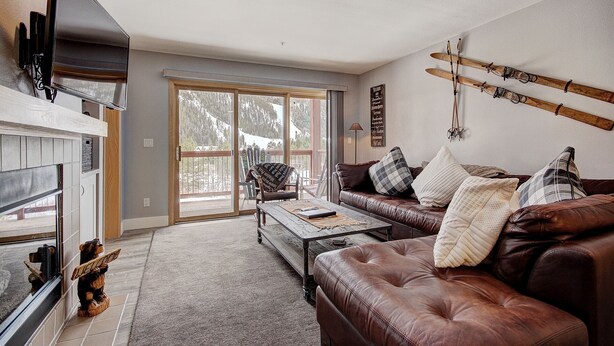 A cozy living room with a fireplace, leather sofa, and a ski rack on the wall. - C212 Cinnamon Ridge 2 Bedroom Condo by RedAwning (Keystone)
