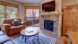 A cozy living room with a stone fireplace, leather sofa, and a flat-screen TV mounted above it. - Amazing Copper Springs Condo With Awesome Views - CS221 by Redawning (Copper Mountain)